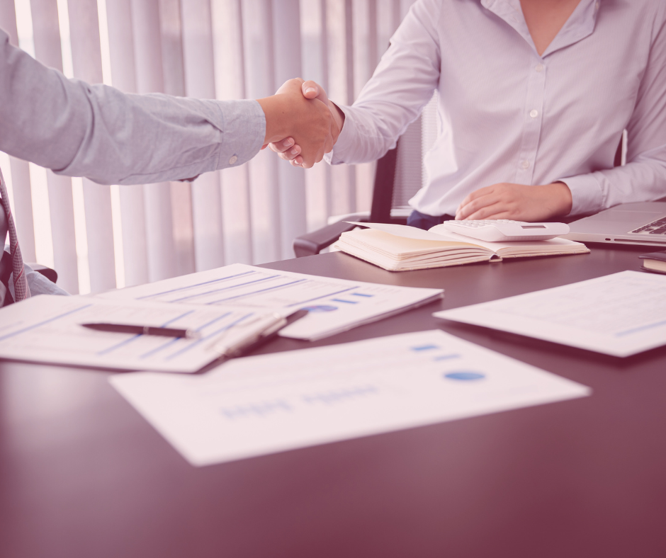 Dos personas dándose la mano para cerrar un trato ante una mesa con papeles